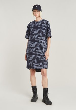 Robe courte navy à manches courtes avec un motif de texte gris audacieux, col rond, coupe décontractée et fentes sur les côtés, assortie à des bottes de combat noires à lacets.