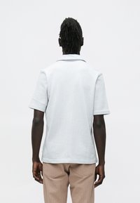 Lyseblå kortermet poloshirt med et strukturert mønster, med klassisk krage og rett kant, kombinert med beige bukser.