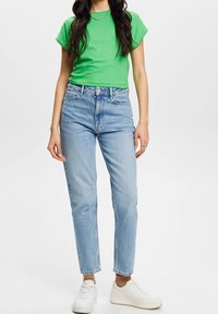 T-shirt verde a maniche corte abbinato a jeans a vita alta blu. I jeans hanno una vestibilità dritta e sono leggermente sbiaditi, completati da sneakers bianche.
