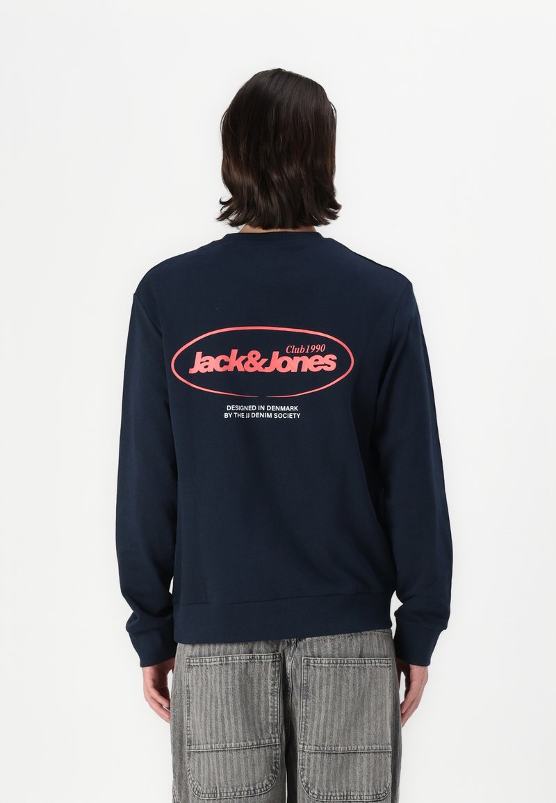 Marineblaue Sweatshirt mit gerippten Bündchen und Saum, auf dem Rücken mit einem großen roten Logo "Jack & Jones Club1990" bedruckt. Aus Baumwollmaterial.