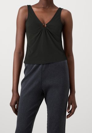 Sort tanktop med V-udskæring og et centralt tvistdetalje med et lille metalaccent. Kombineret med mørke ribbede bukser med vidde.