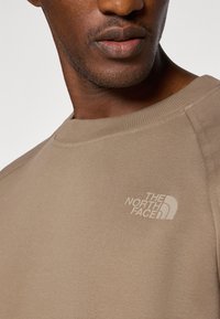 Beige sweatshirt gemaakt van textuurstof, met een ronde halslijn en een klein, lichtgekleurde logo op de borst.