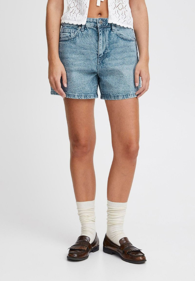 Shorts in denim azzurro con orlo sfilacciato, caratterizzati da un classico design a cinque tasche e passanti per cintura. Abbinati a mocassini marroni e calzini bianchi.