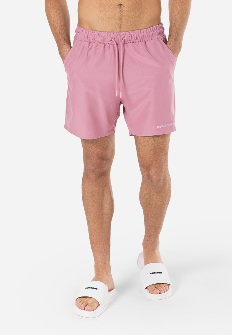 Pantaloni scurți de înot roz deschis, cu un talie elastică și un șnur ajustabil. Prezintă logo-ul "PEGADOR" scris cu litere albe pe lateral.