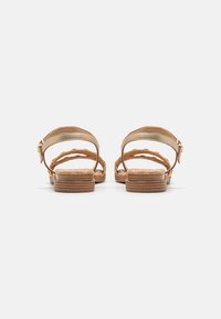 Hellbraune geflochtene Sandalen mit einer glatten braunen Sohle. Ausgestattet mit einer goldenen Metall-Schnalle und einem offenen Fersenbereich. Strukturierter Fußbett für Komfort.