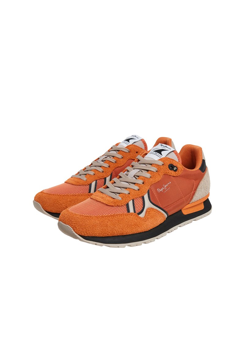 Un par de zapatillas casuales naranjas y beige con cordones grises, rayas en blanco y negro, y detalles de marca sobre un fondo blanco.