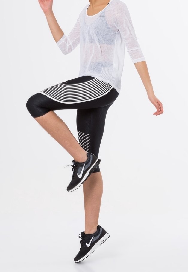 Black athletic leggings with horizontal white stripes, paired with a sheer white top and black sneakers. Displaying dynamic pose.