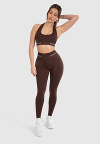 Conjunto de sujetador deportivo y leggings marrones con diseño de cuello halter, cinturilla elástica y acentos de logo blancos en contraste.