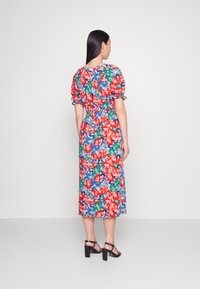 Vestido midi floral em vermelho vibrante, azul, verde e branco. Apresenta mangas balão, um cós elástico e uma saia fluida. Sapatos de salto quadrado pretos.
