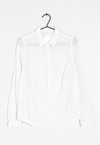 Bílá dlouhá blůza s dlouhými rukávy, s límečkem na knoflíky a malými modrými květinovými vzory. Vyrobena z lehkého, průsvitného materiálu. Zaoblený lem.
