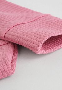 Rosa gerippter Stoff mit einer weichen Textur, zeigt gefaltete Kanten und Nähte. Das Material erscheint leicht und flexibel.