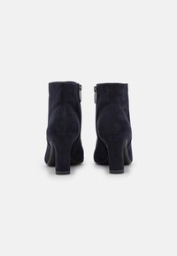 Botines de ante azul marino con un tacón de bloque de 7 cm y cremalleras laterales, que presentan una textura suave y un diseño limpio y moderno.