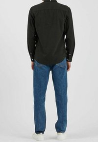 Chemise noire à manches longues avec col boutonné, associée à un jean en denim bleu. La chemise présente un tissu texturé et un ourlet arrondi.