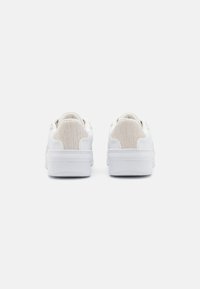 Sneakers bianchi con un retro beige testurizzato, parte superiore liscia, colletto imbottito e suola in gomma. Design minimalista senza loghi visibili.