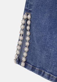 Denim w prostym kroju, ozdobiony dekoracyjnym wykończeniem z sztucznych pereł i metalicznych akcentów wzdłuż bocznego szwu. Niebieski kolor o miękkiej teksturze.