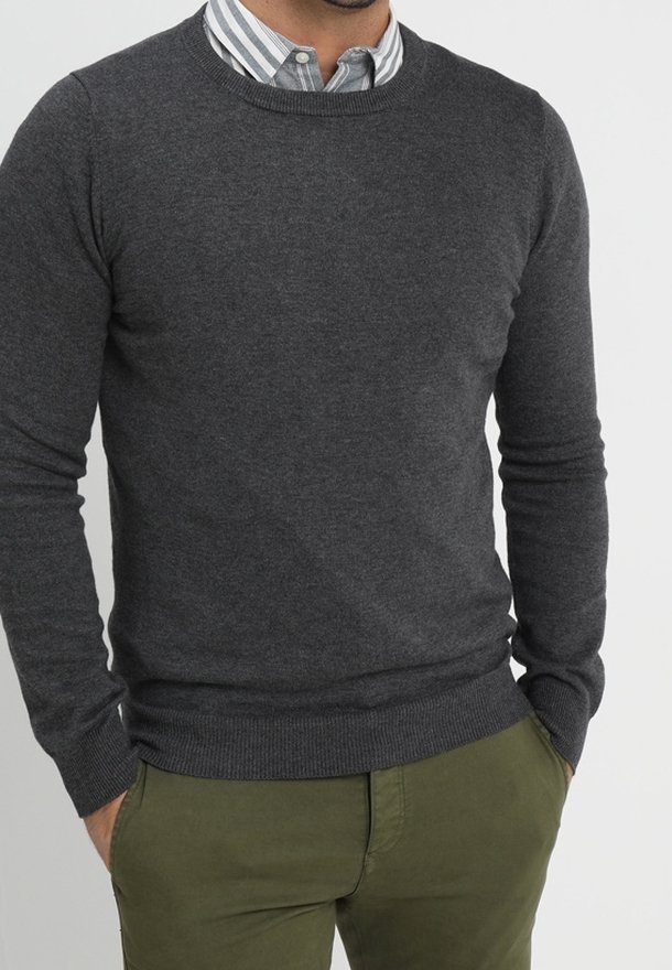 Dunkelgrauer Pullover mit Rundhalsausschnitt aus weichem Strickstoff, mit gerippten Bündchen und Saum, getragen über einem hellblau-weiß gestreiften Hemd.