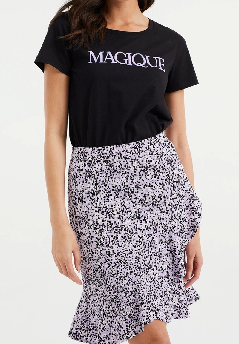 Černé tričko s textem "MAGIQUE", spárované s lilacovou sukní se vzorem černých skvrn a volánkovým lemem. Neformální a vrstvený design.