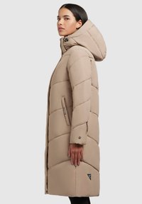 Geacă puffer bej cu glugă, având un design matlasat, buzunare cu fermoar și o etichetă cu logo. Material neted, ușor, cu o croială lejeră.