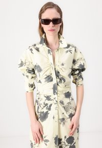 Yellow floral print dress with puffed sleeves, ruched detailing, and button-down front. Model wears dark sunglasses. Smooth fabric texture.