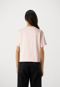 Lys rosa bomull t-skjorte med korte ermer, rund hals og et kort snitt. Bæres med svarte bukser med høy midje som har baklommer.