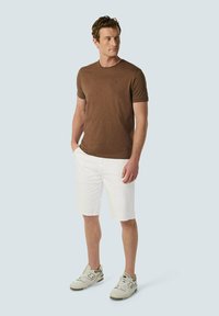 Braunes T-Shirt mit kurzen Ärmeln, weiße knielange Shorts und graue Sneakers. Einfaches Design, einfarbige Farben, lässige Passform, glatte Textur.