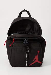 Fekete hátizsák piros részletekkel, kiemelkedő Jumpman logóval. Cipzáras zsebek és tartós szövet anyag jellemzi, valamint egy felső hordozó füle.
