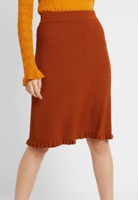 Stickad kjol i rostfärg med ett strukturerat mönster, som har en ribbad midja och volang nertill för extra detalj.