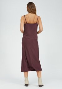 Mauve kaksiosainen asu, jossa on hihaton paita ja pitkä hame, valmistettu sileästä kankaasta. Mallilla on yllä beige nilkkureita.