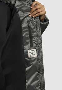 Grå vadderad jackas insida med en dragkedjeficka, som har en tygetikett med text. Slät textur, lätt design och fodrat mönster.