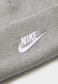 Harmaa neulottu pipo, jossa on ribbitekstuuria. Etuosassa on valkoinen brodeerattu Nike-logo.