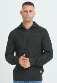 Ciemnoszary sweter robiony na drutach z kołnierzem na pół-zamek, prą�żkowaną fakturą, długimi rękawami i małą naszywką z logo u dołu.