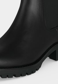 Bottine en cuir noir avec panneau latéral élastique, semelle crantée épaisse et talon bloc bas.