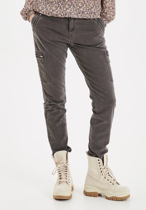Persona che indossa pantaloni cargo grigi aderenti con tasche con zip e borchie e stivali da combattimento beige con lacci e suole spesse.