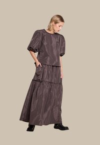 Brun puffermansjort med puffede ermer og lagdelt maxiskjørt laget av glinsende stoff. Har rund hals og sidelommer i skjørtet. Svarte ankelsko.