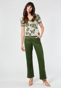 Top de punto verde con estampado de mariposas, de manga corta y escote en V, combinado con pantalones verdes ajustados que tienen rayas laterales. Tacones neutros.