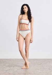 Δίδυμο μπικίνι σε κρεμ χρώμα με μαύρες και κόκκινες λεπτομέρειες. Διαθέτει τοπ μπαντό με λεπτές τιράντες και σλιπ με ψηλή μέση. Ομαλή υφή.