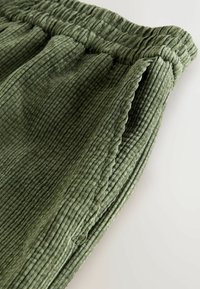 Green ribbed fabric with a textured surface. Features an elastic waistband. The material appears soft and slightly textured, indicating comfort.