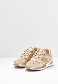 Beige kengät, joissa on teksturoitu kangasyläosa kullan yksityiskohdilla, pyöreä kärki, nauhakiinnitys ja pehmustettu nilkkaosa mukavuutta varten.