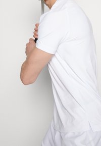 Vit kortärmad polo skjorta i texturerad tyg, med krage och en lätt kurva i fållen, kombinerad med vit shorts.