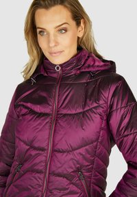 Paarse pufferjas met capuchon, glanzende textuur, rits aan de voorkant en diagonale stiksels. Voorzien van een trekkoord en ritszakken.