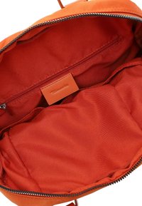 Orange fabric bag interior with a smooth texture, featuring a zippered pocket and a branded leather tag. Spacious design without exterior details.