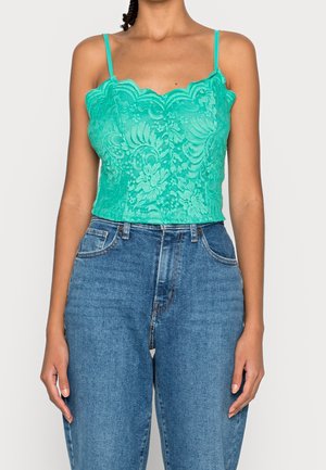 Een tealblauwe kanten hemd met geschulpte randen en dunne bandjes, gecombineerd met high-waisted blauwe spijkerbroek met een lichte wassing en zakken.