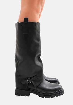 Bottes noires montantes en cuir lisse avec un bout rond, une semelle épaisse et un détail de boucle sur le côté. Elles comportent une languette en haut.