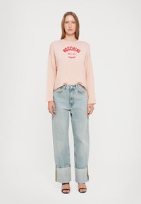 Tee-shirt à manches longues rose clair avec une impression rouge 'Moschino Jeans'. Jean large bleu clair avec des ourlets contrastés. Porté avec des sandales noires.