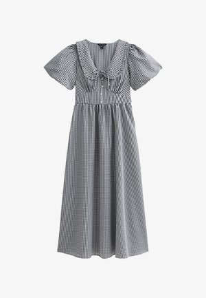 Abito a scacchi bianco e nero con maniche a palloncino corte, un ampio scollo e una vita arricciata, con gonna fino al ginocchio. Caratterizzato da un fiocco al centro.