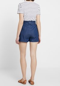 Shorts en denim à taille haute, avec un ourlet effiloché et une ceinture élastique, associés à un t-shirt rayé et des sandales marron.