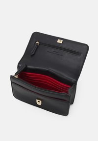 Černá kožená peněženka se zipovou kapsou, několika přihrádkami na karty v červené barvě a zapínáním na zlatou sponu. Hladká textura a kompaktní design.