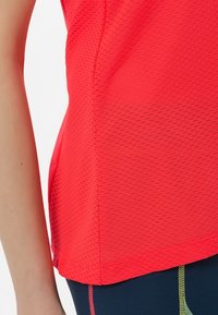Top deportivo coral hecho de una tela texturizada y transpirable. Presenta un diseño ajustado con un dobladillo liso y sutiles acentos reflectantes.
