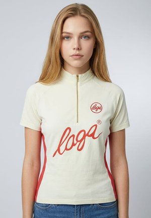 Joven mujer con cabello rubio largo lleva una camiseta beige de manga corta con rayas laterales rojas y texto rojo "loga", de pie frente a un fondo liso.