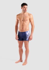 Granatowe trunks kąpielowe z nadrukowanym wzorem po boku, charakteryzujące się gładką fakturą i dopasowanym kształtem, wykonane z lekkiego, elastycznego materiału.
